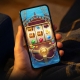 Ilustrasi tangan memegang telefon dengan permainan slot bertema lanun di skrin — mencuba slot secara percuma dengan Cuba Free di Pirate777.